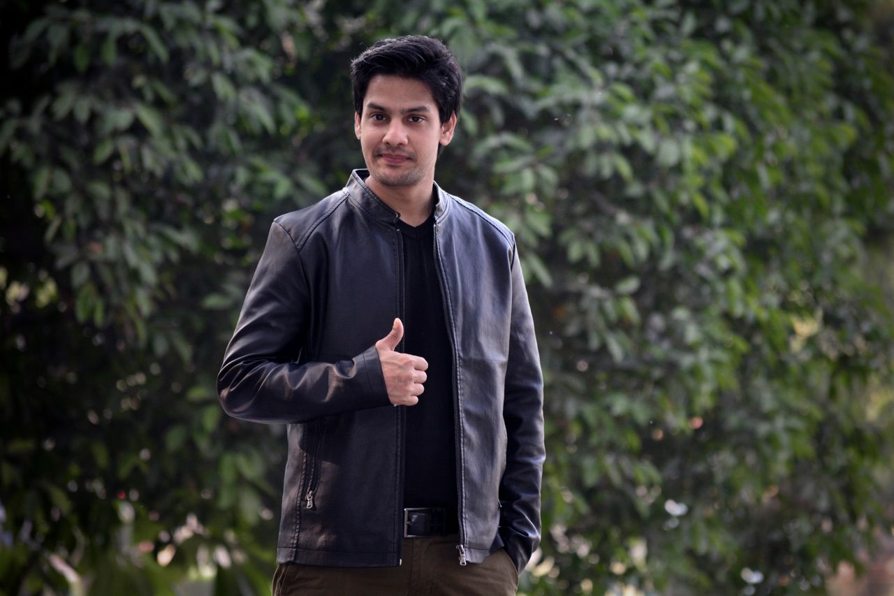 gallery-05 Portrait of a confident young man in a black leather jacket giving a thumbs up outdoors.