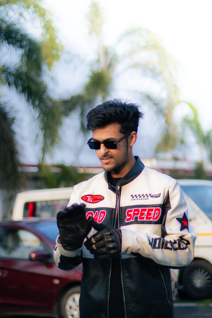 featured-images-01 Young man in sunglasses and 'Road Speed' jacket posing outdoors with palm trees.