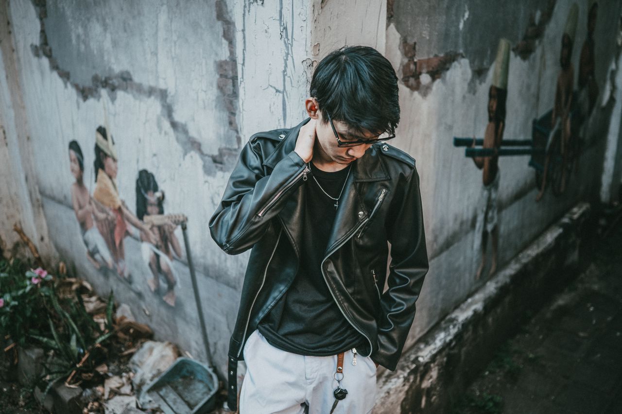 gallery-03 Stylish young man in a leather jacket stands against a mural wall.