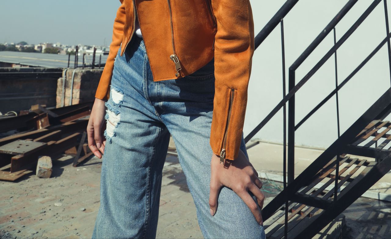 gallery-08 Close-up of a stylish outfit featuring a leather jacket and ripped jeans outdoors.