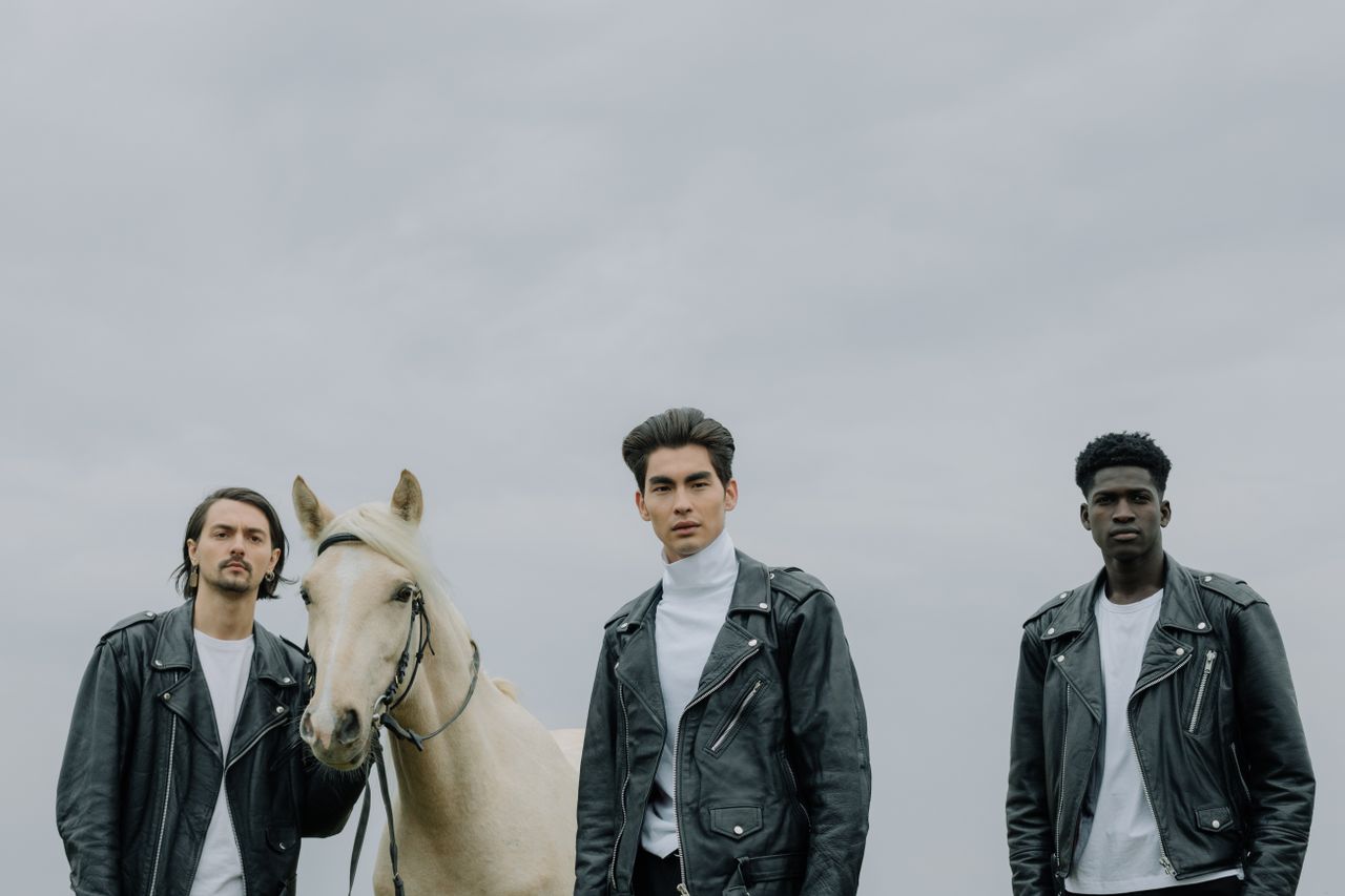 engagement-photography-03 Three men wearing black leather jackets posing with a horse outdoors, showcasing modern fashion.