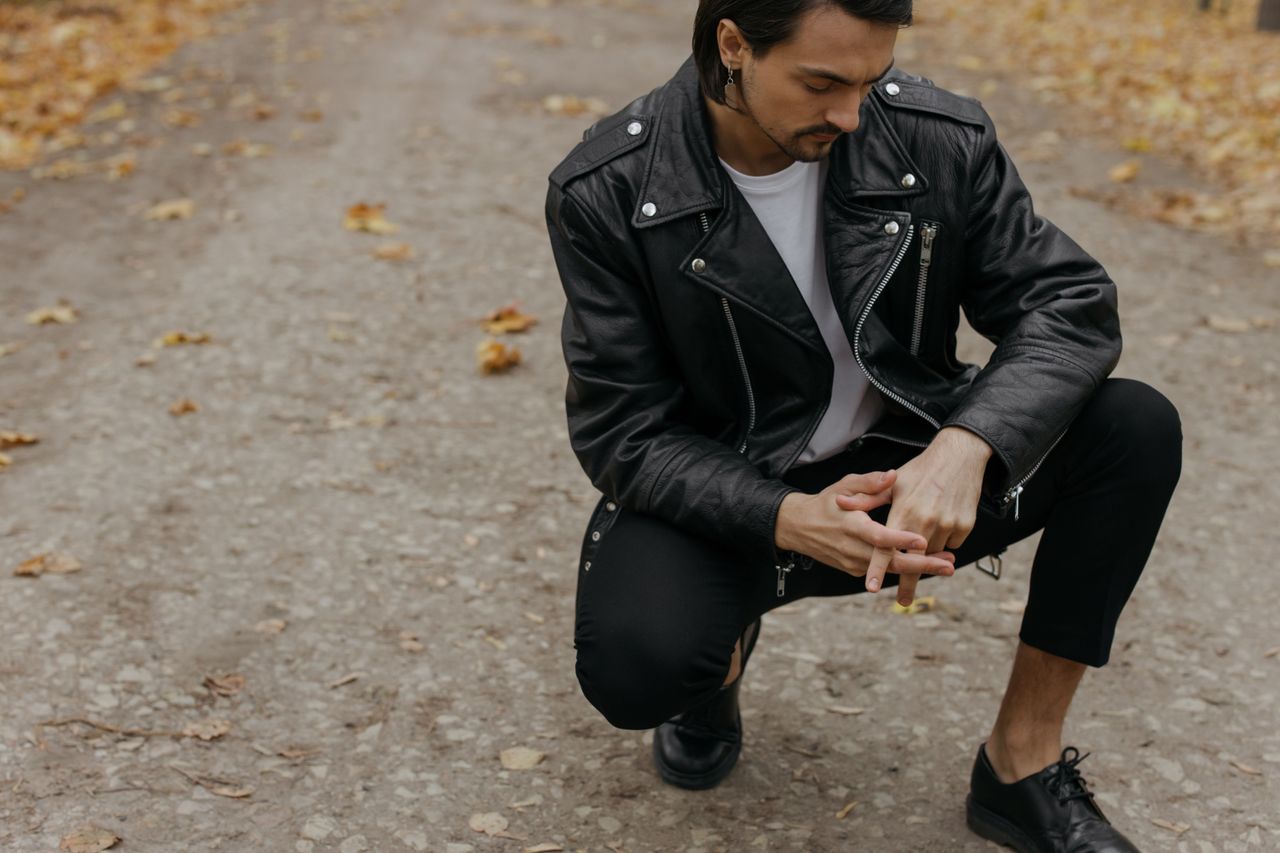 gallery-09 Man squatting on a path wearing a leather jacket, capturing autumn fashion style.