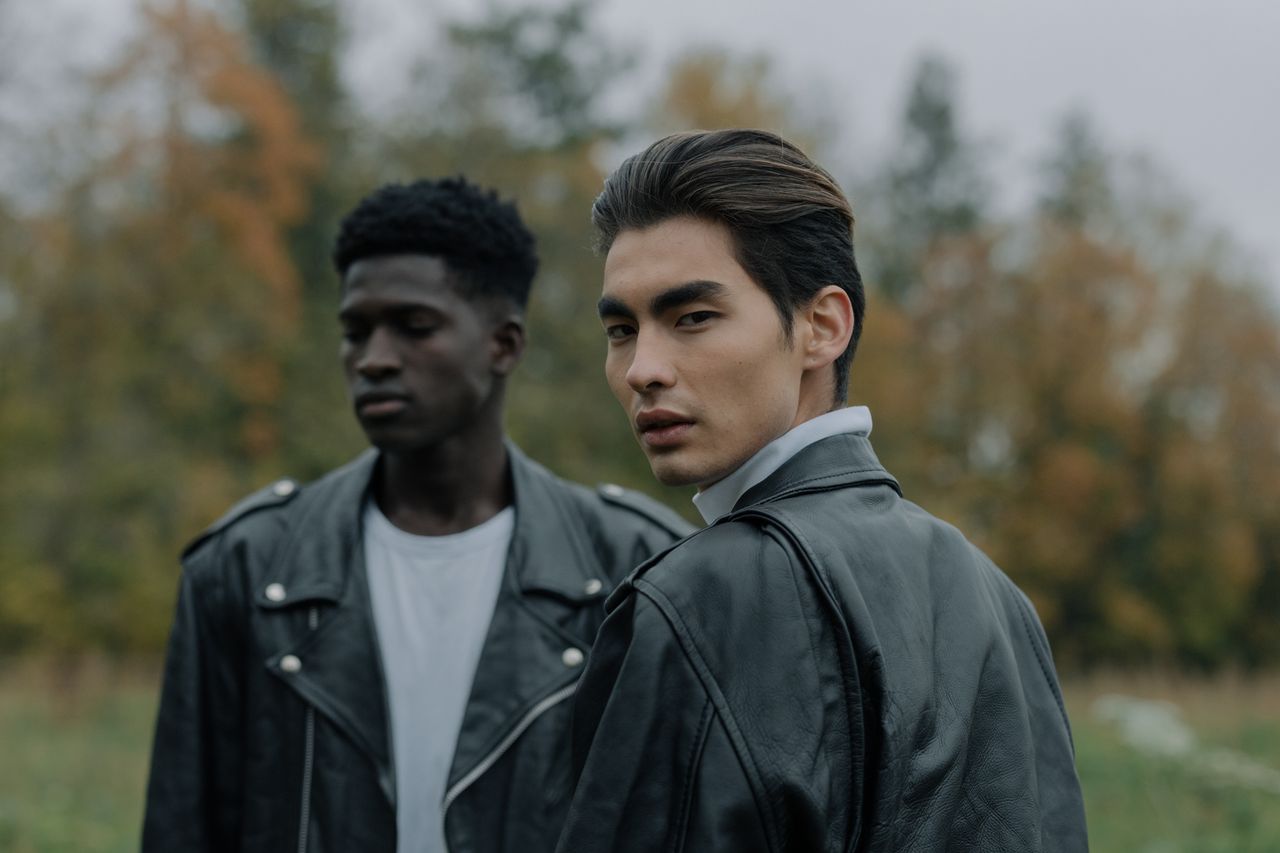 gallery-04 Two stylish men wearing leather jackets outdoors in an autumn setting.